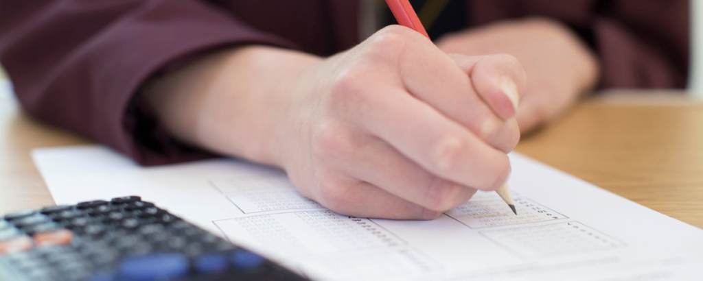 A focused student solving algebra equations on a notebook during GED math prep session.
