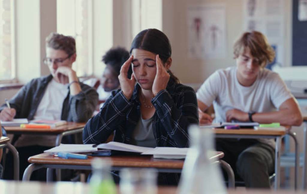 Diverse group of students in a classroom looking frustrated with uniform textbooks.